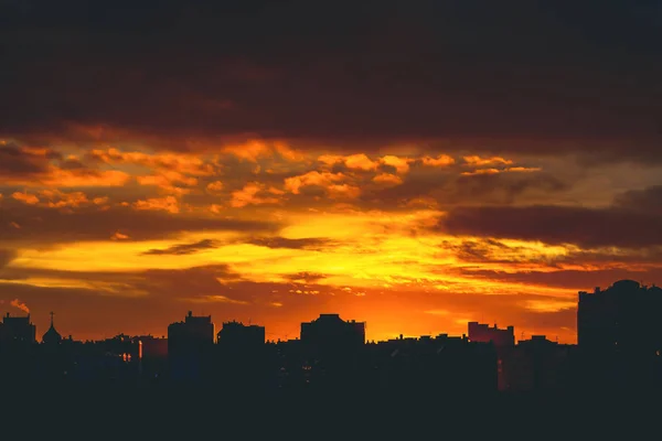 城市景观与生动的火光的黎明 令人惊叹的温暖戏剧性多云的天空以上的城市建筑的黑暗的轮廓 橙色的阳光 阴天中日出的大气背景 复制空间 — 图库照片