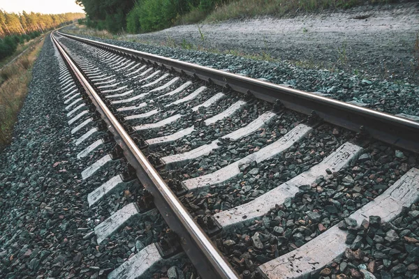 Background of diagonal railroad at dusk with copy space. Rails, sleepers, fastenings and crushed stone close up. Railway traveling. Journey on rail track to sunlight. Pattern in dark blue tones.