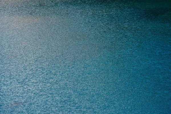 Amazing textured background of calm cobalt clean water surface in evening. Sunshine reflected in mountain lake close up. Beautiful ripples on shiny blue water in morning. Wonderful relax texture.