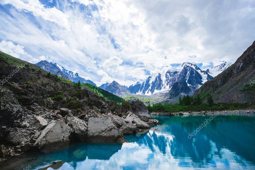 Mountain lake is surrounded by large stones and boulders on front of giant beautiful glacier. Amazing snowy mountains. Ridge with snow. Wonderful atmospheric landscape of majestic nature of highlands.