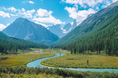 Güzel buzul önce vadide Serpentine nehri. Kozalaklı ormanı olan dağların arkasındaki karlı kayalar. Mavi gökyüzünün altında dev karlı dağ tepesinde büyük bulutlar. Yayla doğasının atmosferik manzarası.