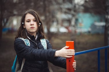 Sırt çantası ile Schoolgirl yağmurda bulutlu havalarda şehir sokak boyunca depresif devlet yürüyor. Soluk tonlarda ıslak saçlı kulaklıklı genç kız, fotokopi alanı ile açık havada. Melankolik genç.