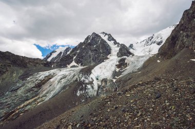 Bulutlu gökyüzü altında karlı dev dağ aralığı. Kar lı kayalık sırt. Büyük bir buzul. Su akıntıları ile buzlu dağ. Harika dağlar. Doğanın atmosferik minimalist dağlık manzara.
