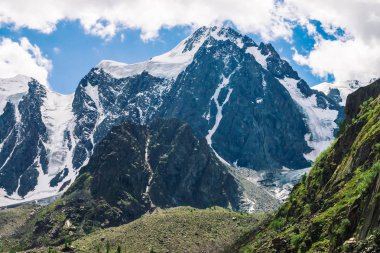 Bulutlu mavi gökyüzü altında büyük dağ yamacıarkasında karlı dev dağlar. Kar lı kayalık sırt. Büyük bir buzul yakın. Yaylaların görkemli doğasının atmosferik minimalist dağlık manzarası.