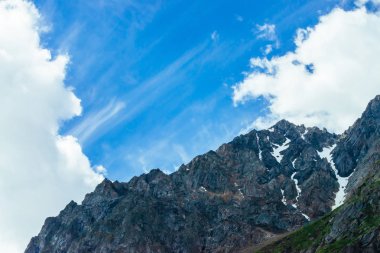 Tepenin üstündedev bulutlar var. Kar ile alışılmadık kayalık dağ. Mavi bulutlu gökyüzü altında Amazing dağ aralığı. Sniwy uçurum. Harika büyük kayalar. Yaylaların görkemli doğasının atmosferik manzarası.