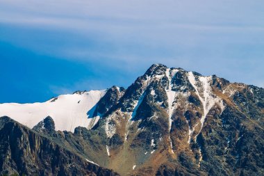 Mavi berrak gökyüzünde karlı dağ tepesinde. Güneşli bir günde bulutların altında kayalık sırt. Görkemli doğanın atmosferik minimalist manzara.