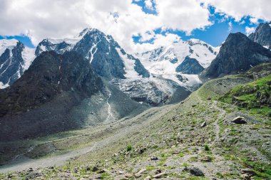 Yürüyüş parkuru güneşli bir günde büyük karlı dağlara yol açar. Güneş ışığında harika bir buzul. Dağdaki su akıntıları. Yaylaların zengin bitki örtüsü. Doğanın atmosferik güneşli minimalistler manzara.