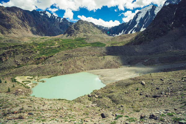 Горное озеро в форме кометы возле огромных скалистых гор. Удивительные снежные горные хребты. Прекрасный гигантский ледник под облачным голубым небом. Атмосферный космический ландшафт величественной природы высокогорья
.