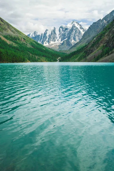 Shine water in mountain lake in highlands. Wonderful giant snowy mountains. Creek flows from glacier. White clear snow on ridge. Amazing atmospheric landscape of majestic Altai nature.