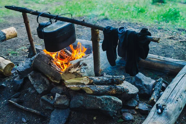 Drying wet clothing on the bonfire during camping. Socks drying on fire. Cauldron and kettle above campfire. Cooking of food on nature. Firewood and branches in fire. Active rest in forest.