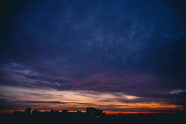 Canlı sıcak şafak ile Cityscape. Şehir binalarının karanlık siluetleri üzerinde Amazing dramatik mavi mor bulutlu gökyüzü. Turuncu güneş ışığı. Bulutlu havalarda gün doğumunun atmosferik arka planı. Kopyalama alanı.