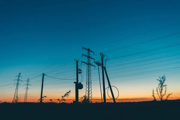 日出背景的字段中的电源线 黎明时分用电线的电线杆的剪影 暖橙色蓝天上的高压电缆 日落时分的电力行业 许多电缆在风景如画的生动的天空 — 图库照片