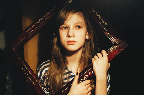 Portrait of a sad little girl looking out of a wooden frame. Child. Atmospheric photography. Conceptual.