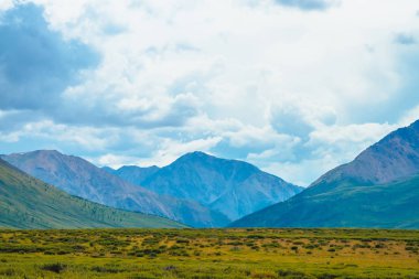 Bulutlu gökyüzü altında dev dağların muhteşem görünümü. Bulutlu havalarda büyük bir dağ sırası. Harika vahşi manzara. Görkemli doğanın atmosferik dramatik yayla manzara. Doğal dağ manzarası.
