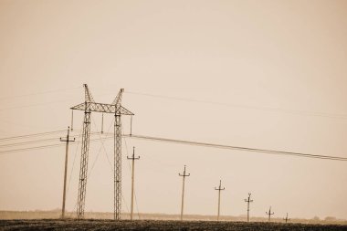 Sepya tonlarında gökyüzünün altında alan da güç hatları ile atmosferik manzara. Fotokopi alanı ile elektrik kulesi arka plan görüntüsü. Yerden yüksek voltajlı kablolar. Tek renkli elektrik endüstrisi.