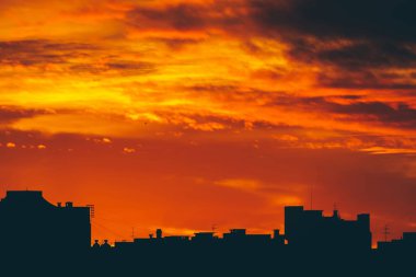 Cityscape canlı ateşli şafak ile. İnanılmaz sıcak dramatik bulutlu gökyüzü karanlık siluetleri şehir binaların yukarıda. Turuncu güneş ışığı. Gündoğumu bulutlu havalarda atmosferik arka plan. Kopya alanı.