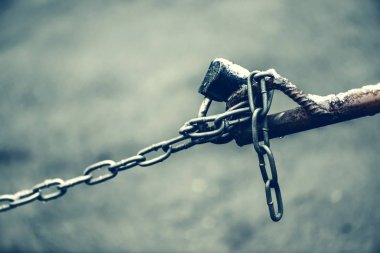 Kahverengi çit zinciri üzerinde kapalı asma kilit kopya alanı ile bokeh ile asfalt arka plan üzerinde yakın çekim. Park yeri kilidi ile fon. Mavi soluk tonlarda kontrol noktası görüntüsü.