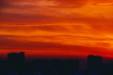 Cityscape canlı ateşli şafak ile. İnanılmaz sıcak dramatik bulutlu gökyüzü karanlık siluetleri şehir binaların yukarıda. Turuncu güneş ışığı. Gündoğumu bulutlu havalarda atmosferik arka plan. Kopya alanı.