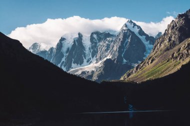 Mavi gökyüzünün altında inanılmaz bir buzul. Karla kaplı dağ sırası. Dev harika karlı dağlarda dev bulut. Mat tonlarda yaylaların görkemli doğasının atmosferik minimalist karamsar manzarası.