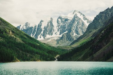 Muhteşem, dev, karlı dağlar. Nehir buzuldan dağ gölüne akar. Dağlık arazide parlayan su. Tepede beyaz kar var. Muhteşem atmosferik Altai doğası..