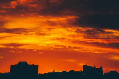 Cityscape canlı ateşli şafak ile. İnanılmaz sıcak dramatik bulutlu gökyüzü karanlık siluetleri şehir binaların yukarıda. Turuncu güneş ışığı. Gündoğumu bulutlu havalarda atmosferik arka plan. Kopya alanı.