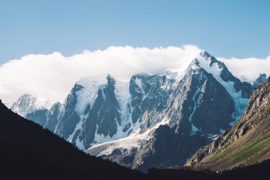 Mavi gökyüzünün altında inanılmaz bir buzul. Karla kaplı dağ sırası. Dev harika karlı dağlarda dev bulut. Mat tonlarda yaylaların görkemli doğasının atmosferik minimalist karamsar manzarası.