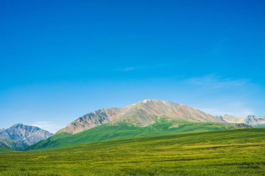 Berrak mavi gökyüzü altında yeşil vadi üzerinde kar ile dev dağlar. Güneş ışığında yaylaların zengin bitki örtüsü ile Çayır. Görkemli doğanın inanılmaz güneşli dağ manzara.