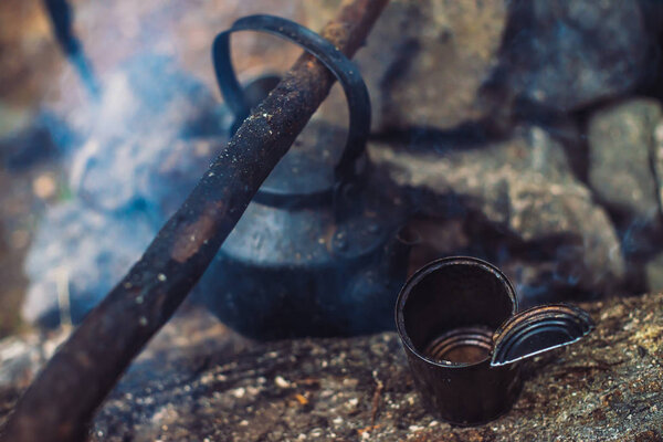 Extinguished bonfire with kettle on large firewood. Extinct bonfire close-up. Abandoned camping in dusk. Forest abode of homeless. No fire. Active outdoor recreation in twilight. Fresh air on nature.