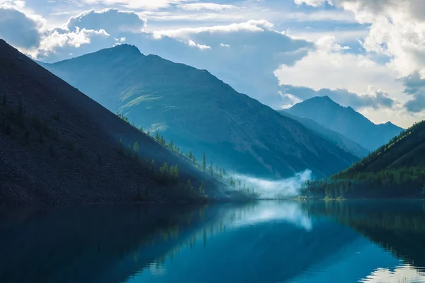 早朝の高地の幽霊山湖 澄んだ水面に映る山や雲の美しい霧のシルエット キャンプファイヤーの煙雄大な自然の素晴らしい風景 — ストック写真