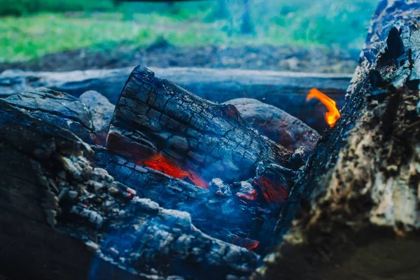 Smoldered logs burned in vivid fire close up. Atmospheric background with orange flame of campfire. Unimaginable detailed image of bonfire from inside with copy space. Smoke and glowing embers in air.