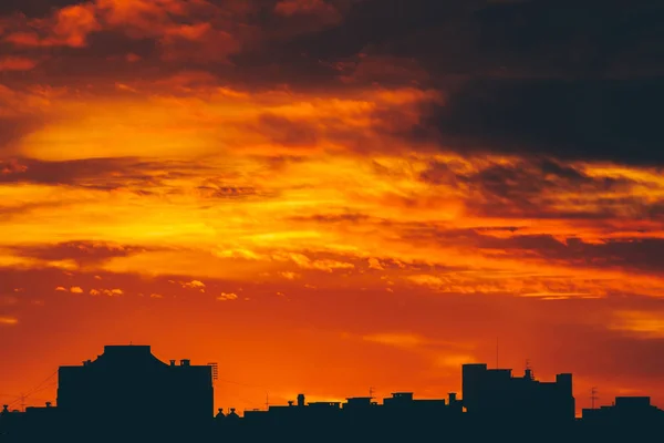 Cityscape canlı ateşli şafak ile. İnanılmaz sıcak dramatik bulutlu gökyüzü karanlık siluetleri şehir binaların yukarıda. Turuncu güneş ışığı. Gündoğumu bulutlu havalarda atmosferik arka plan. Kopya alanı.