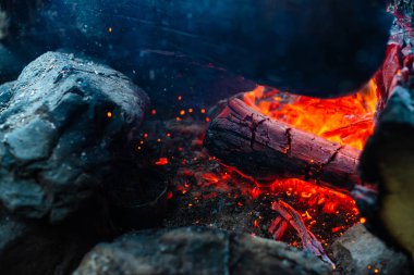 Yanan kütükler canlı ateşte yakılır. Kamp ateşi turuncu alev ile atmosferik arka plan. Kopya alanı ile içeriden şenlik ateşi hayal edilemez ayrıntılı görüntü. Havada duman ve parlayan közler.