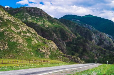 Güneş ışığında geçen dağ yolu. Dev dağların eteklerinde asfalt yol. Görkemli doğanın inanılmaz renkli yayla manzara.