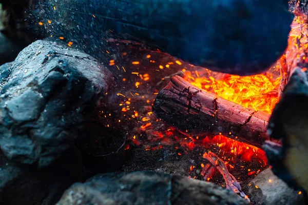 鮮やかな火の中で焼かれた解体されたログを閉じます キャンプファイアの炎と大気中の背景 コピースペースと内側からたき火の想像を絶する詳細なイメージ 煙と輝くメンバーの渦 — ストック写真