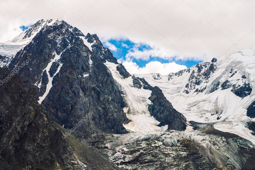 Amazing huge glacier top. Snowy mountain range in cloudy blue sky. Wonderful giant rocky ridge with snow. Atmospheric minimalist landscape of majestic nature of highlands. Tranquil mountainscape.