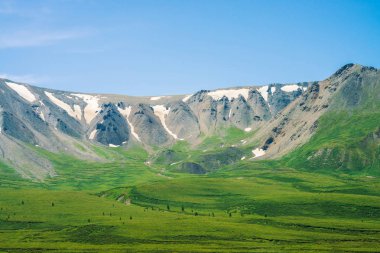 Güneşli bir günde yeşil vadinin üzerinde kar ile dev dağlar. Zengin bitki örtüsü ve güneş ışığında dağlık ağaçlar ile Çayır. Görkemli doğanın muhteşem dağ manzarası.