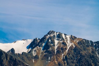 Mavi berrak gökyüzünde karlı dağ tepesinde. Güneşli bir günde bulutların altında kayalık sırt. Görkemli doğanın atmosferik minimalist manzara.