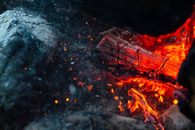 Yanmış odunlar yakın çekim ateşinde yanmış. Atmosferik arka plan ve kamp ateşi. İçeriden kopyalanmış şenlik ateşinin tasavvur edilemez detaylı görüntüsü. Duman fırtınası ve parlayan közler..