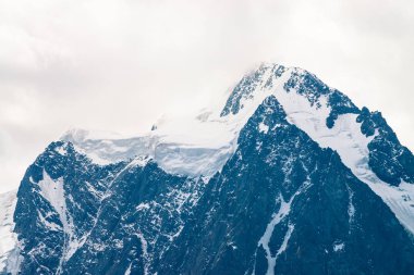 İnanılmaz büyük bir buzul tepesi. Bulutlu gökyüzünde karlı dağ sırası. Sis içinde kar ile harika dev kayalık sırt. Yaylaların görkemli doğasının atmosferik minimalist manzarası. Sakin dağ manzarası.