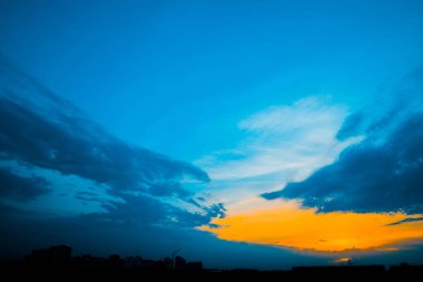 Şehir binalarının siluetleri arkasında atmosferik mavi bulutlu gökyüzü. Kobalt ve kopya alanı için yoğun bulutlar ve parlak sarı güneşli ışık ile gündoğumu turuncu arka plan. Bulutların üzerindeki Siyam cenneti.
