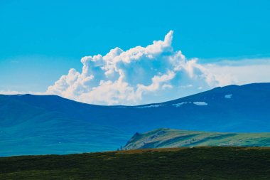 Karla dolu dev dağların muhteşem manzarası. Dağın üzerinde büyük bir bulut. Uçurumun üstündeki büyük kayalık kayalık. Harika vahşi manzara. Görkemli doğanın atmosferik yayla manzarası. Doğal dağ manzarası.