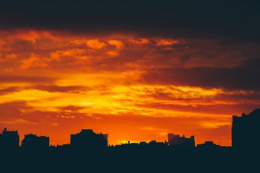 Cityscape canlı ateşli şafak ile. İnanılmaz sıcak dramatik bulutlu gökyüzü karanlık siluetleri şehir binaların yukarıda. Turuncu güneş ışığı. Gündoğumu bulutlu havalarda atmosferik arka plan. Kopya alanı.