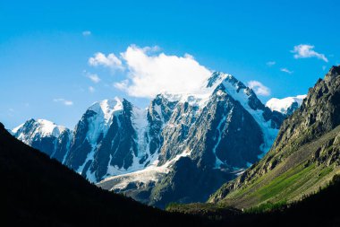 Mavi gökyüzünün altında inanılmaz bir buzul. Güneş ışığında dev harika karlı dağlarda dev bulut. Zengin bitki örtüsü ve yayla ormanı. Güneşli bir günde görkemli doğanın atmosferik minimalist manzara.