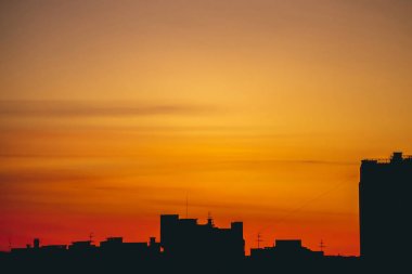 Canlı ateşli şafak ile Cityscape. Şehir bina çatıların karanlık siluetleri üzerinde Amazing sıcak dramatik bulutlu gökyüzü. Turuncu kırmızı güneş ışığı. Bulutlu havalarda gün doğumunun atmosferik arka planı. Kopyalama alanı.