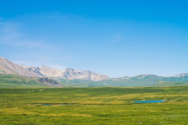 Berrak mavi gökyüzü altında yeşil vadi üzerinde kar ile dev dağlar. Zengin bitki örtüsü ve güneş ışığında dağlık göller ile Çayır. Görkemli doğanın inanılmaz güneşli dağ manzara.