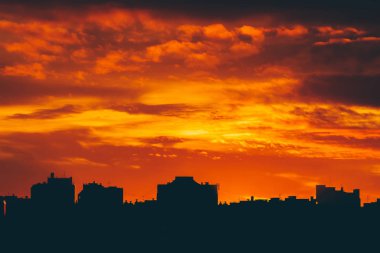 Cityscape canlı ateşli şafak ile. İnanılmaz sıcak dramatik bulutlu gökyüzü karanlık siluetleri şehir binaların yukarıda. Turuncu güneş ışığı. Gündoğumu bulutlu havalarda atmosferik arka plan. Kopya alanı.