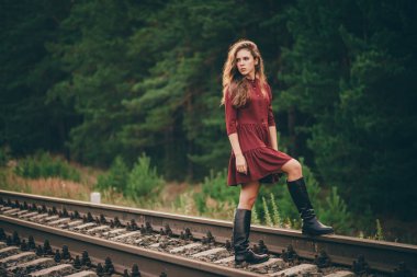 Demiryolu üzerinde ormanda doğada kıvırcık doğal saçları ile Güzel üzgün düşünceli kız. Bordo elbiseli hayalperest bayan demiryolunda yürüyor. Şafakta rayların üstünde ki depresif kız. Sonbaharda saçta güneş. Kötü ruh hali.