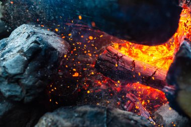 Yanmış odunlar yakın çekim ateşinde yanmış. Atmosferik arka plan ve kamp ateşi. İçeriden kopyalanmış şenlik ateşinin tasavvur edilemez detaylı görüntüsü. Duman fırtınası ve parlayan közler..