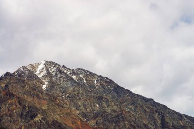 Bulutlu gökyüzünde karlı dağ başı. Bulutların altındaki kayalık sırt. Dağlık bölgelerde bulutlu hava. Görkemli doğanın atmosferik minimalist manzara.