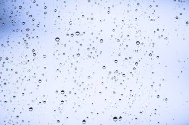Yağmur damlalarıyla kirli pencere camı. Yağmur damlaları ile atmosferik mavi ışık arka plan. Damlacıklar ve lekeler kapanır. Kopyalama alanı ile makroda ayrıntılı saydam doku. Yağmurlu hava.